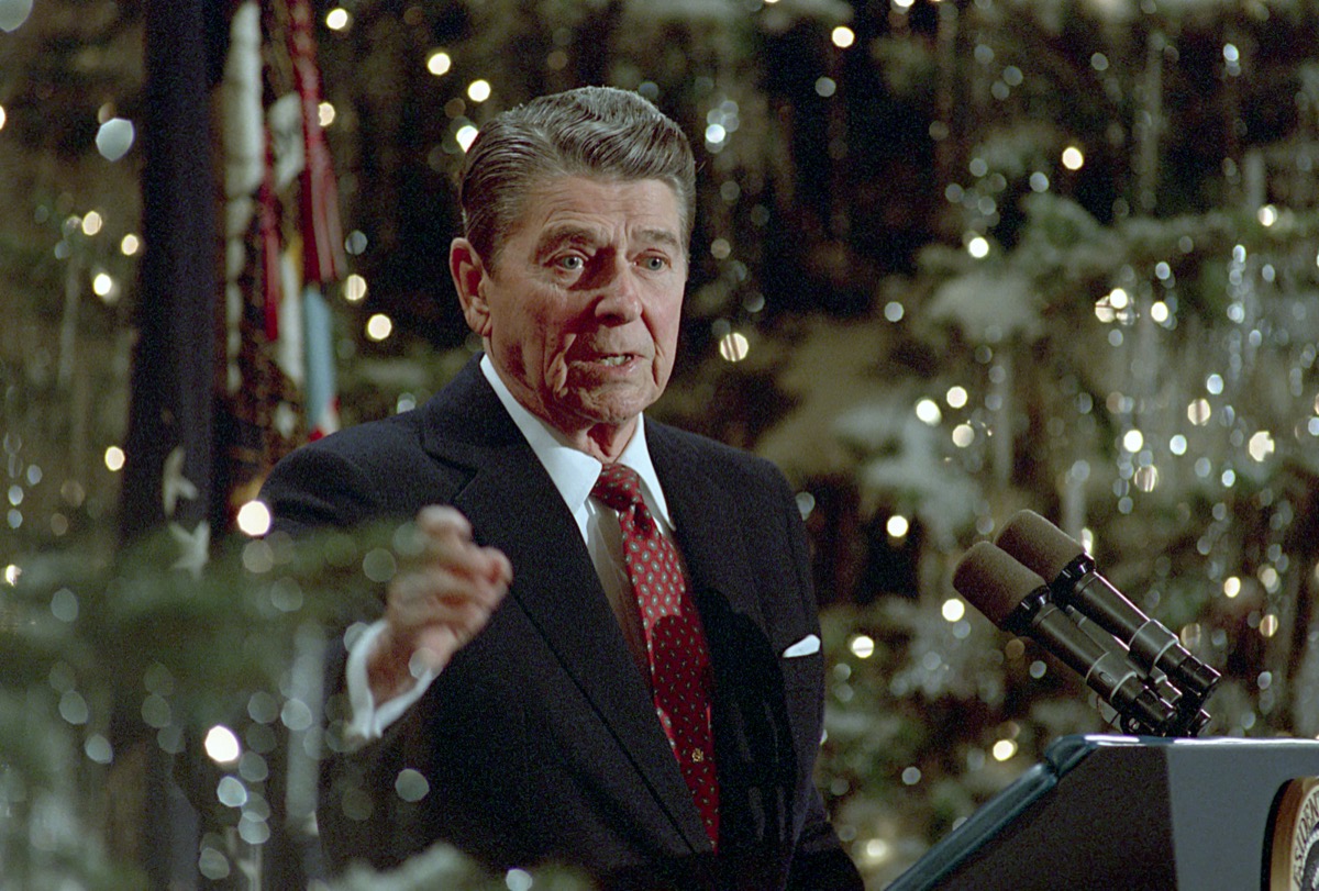 President Ronald Reagan speaking at the podium during a press conference in the East Room of the White House