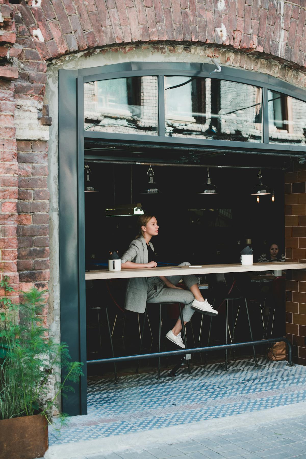 Staged photograph of a woman sitting in a cafe, gazing through a large window — evoking Hannah Starkey's cinematic tableaux of women in everyday urban settings