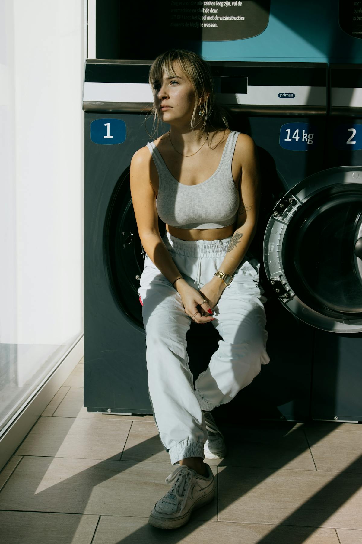 Young woman sitting contemplatively by washing machines in a launderette — reflecting Hannah Starkey's interest in the communal, transitional spaces of women's daily lives