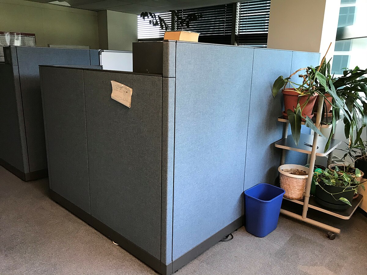 A solitary cubicle in an urban high-rise office building, capturing the isolation of corporate work life