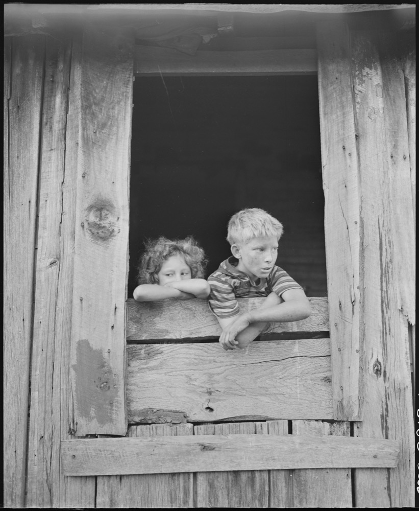 Documentary photograph of figures at a window, evoking domestic intimacy and family history