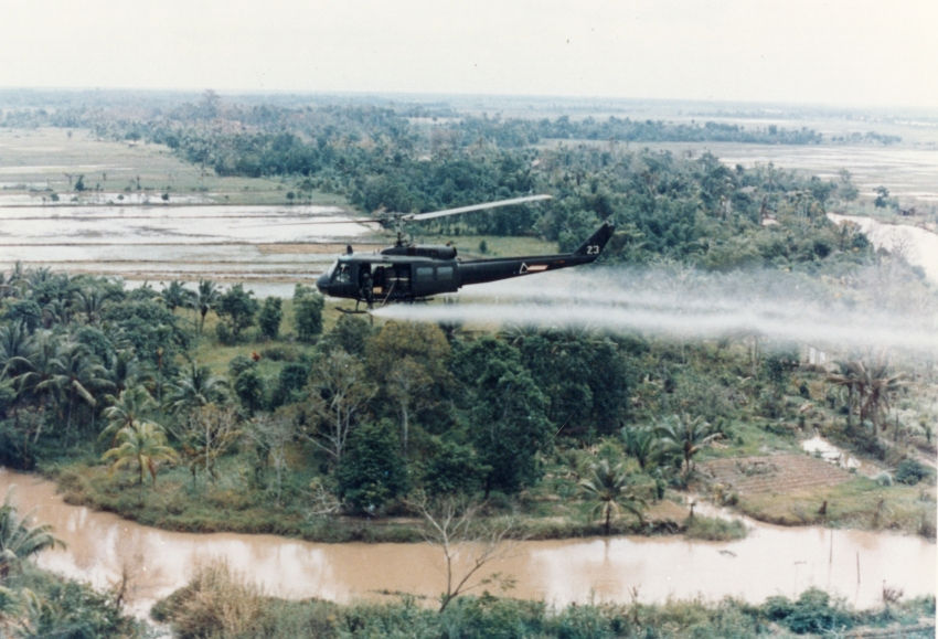 US Huey helicopter spraying Agent Orange over Vietnamese landscape