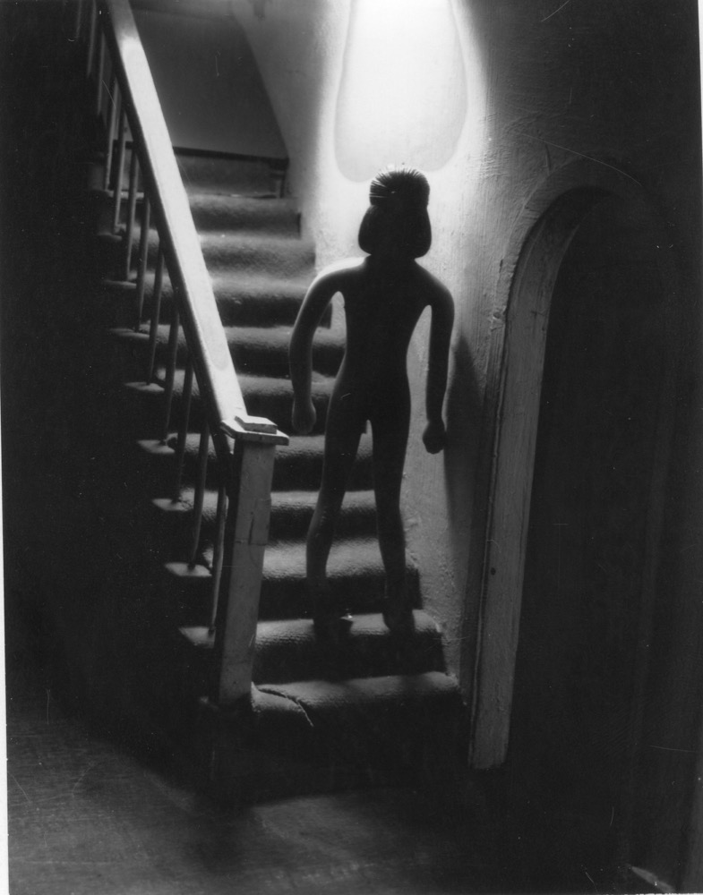 Surreal figure on staircase, evoking Meatyard's staged uncanny scenes with dolls and masks
